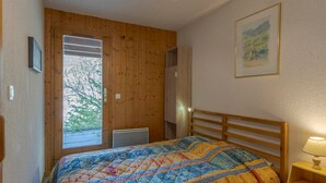 A bedroom with a wooden headboard, a bed with a colorful quilt, a bedside lamp, and a window with a view of trees.