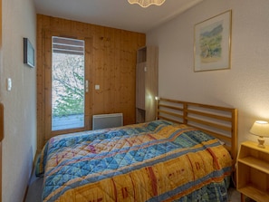 Un dormitorio con cabecera de madera, cama con colcha colorida, lámpara de noche y ventana con vista a árboles.