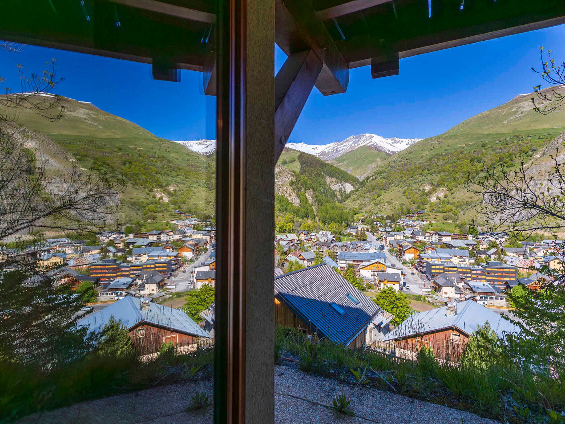 A mountain village with traditional buildings, a clear sky, and snow-capped mountains in the background.