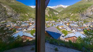 A mountain village with traditional buildings, a clear sky, and snow-capped mountains in the background.