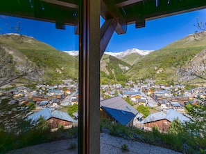 Un pueblo de montaña con edificios tradicionales, cielo despejado y montañas nevadas al fondo.