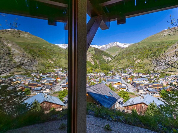 A mountain village with traditional buildings, a clear sky, and snow-capped mountains in the background.