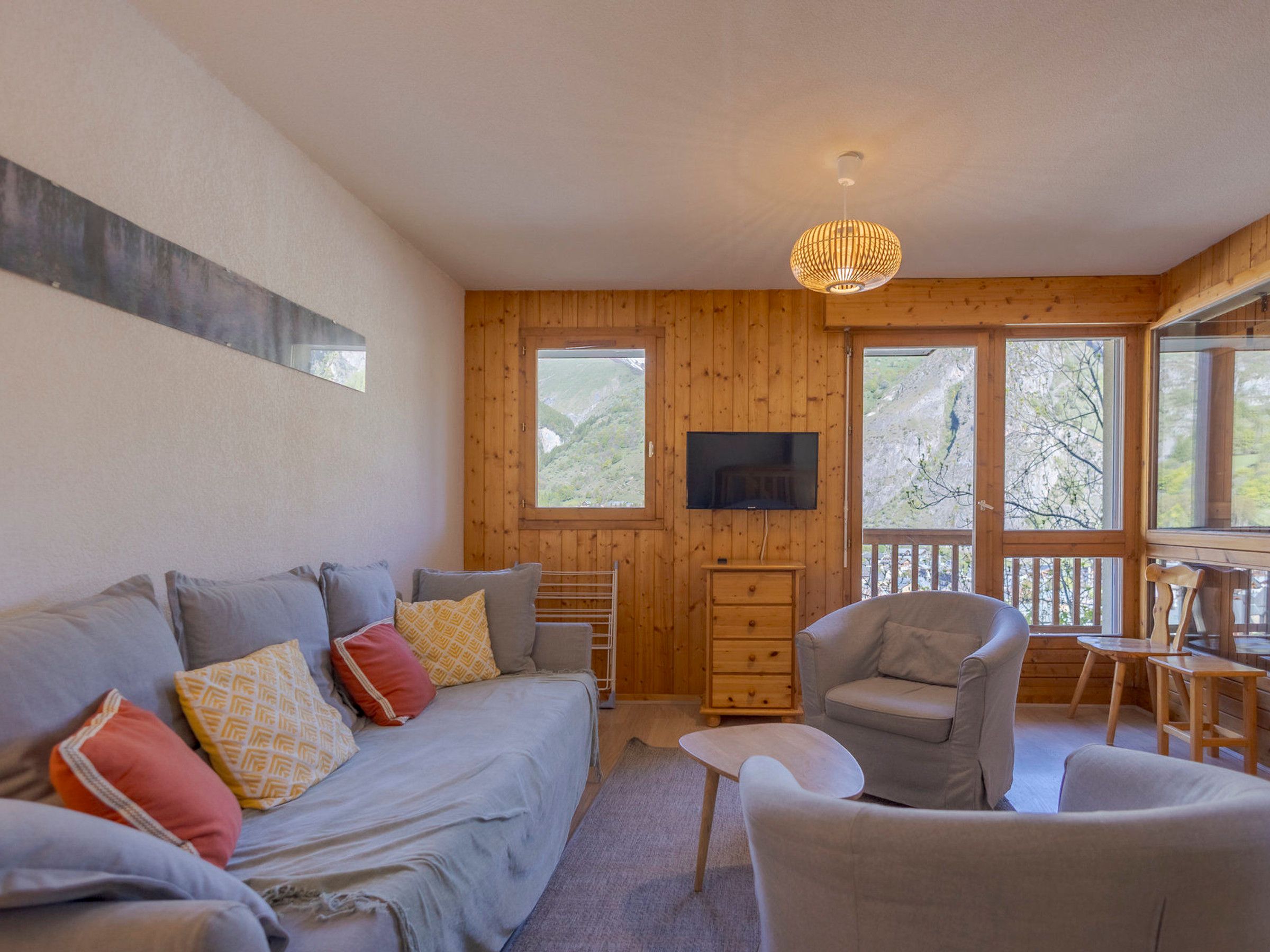 A cozy room with a sofa, armchair, and a television on the wall.