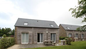 A two-story building with a sloped roof, large windows, and a picnic table in the front yard. - Holiday house in La Hague with pets allowed (La Hague)