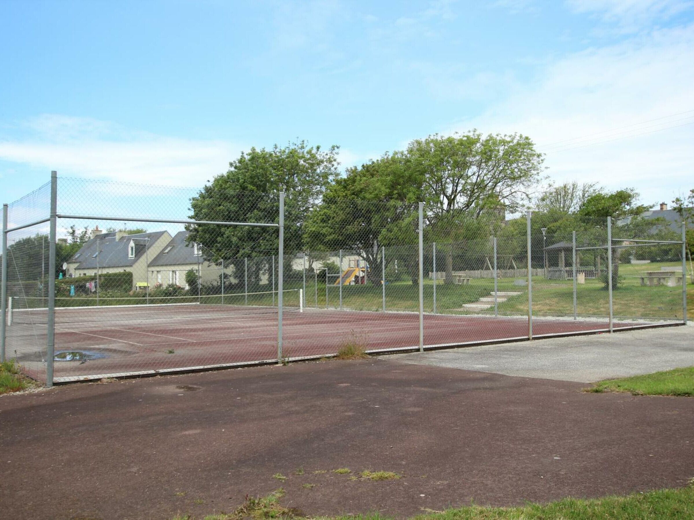 Un terrain de sport clôturé, doté d’une surface rouge, entouré d’une clôture en treillis métallique et d’arbres.