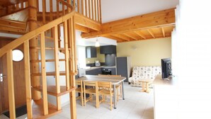 A wooden staircase leading to a loft bedroom, a kitchen with modern appliances, and a living area with a sofa and TV. - Holiday house in La Hague with pets allowed (La Hague)