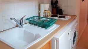 Une cuisine avec un évier blanc, un égouttoir à vaisselle vert, une machine à café et un lave-linge.