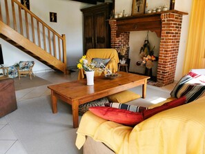 A cozy living room with a wooden staircase, a brick fireplace, and a yellow sofa.