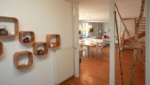 A modern interior with wooden shelves on the wall, a dining area with a white table and chairs, and a wooden staircase. - bloch duplex 165m2 city center 4br3bth (Colmar)
