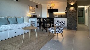 Un soggiorno moderno con un divano, una poltrona fantasia, un tavolino e una zona cucina con bancone.