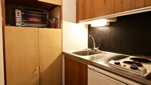 A compact kitchen with wooden cabinets, a stainless steel sink, and a white stove.
