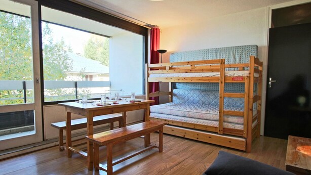 A cozy room with a bunk bed, a wooden table with chairs, a bench, and a sofa.