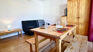 A wooden dining table set with plates, glasses, and cutlery, a bench, a black sofa, and a wooden cabinet.