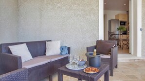 Un canapé en osier avec des coussins, une petite table avec une bouteille et des verres, et une chaise avec un coussin.
