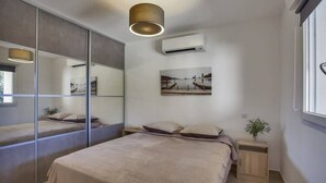 Une chambre moderne avec un grand lit, une table de chevet, un miroir, un appareil de climatisation et une fenêtre.
