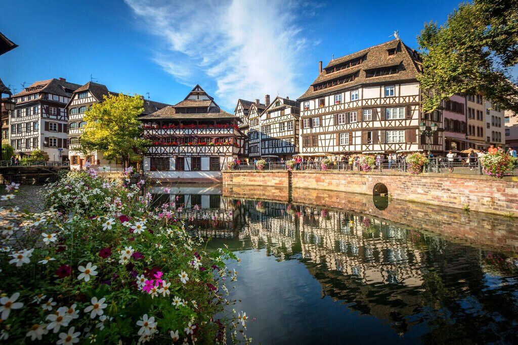 A traditional European town with half-timbered buildings, a canal, and a bridge.