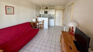 A compact living space with a red sofa, a wooden TV stand, and a kitchen area in the background.