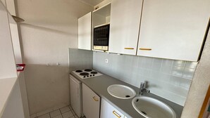 A compact kitchen with white cabinets, a stove, a sink, and a small refrigerator.