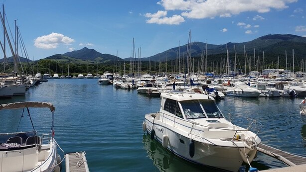 A marina with multiple boats docked, a clear sky, and mountains in the background.