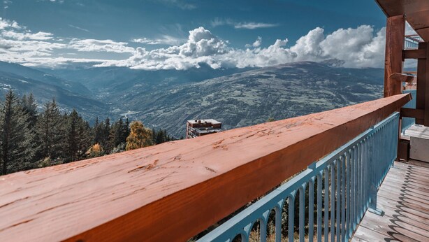 A wooden balcony with a blue railing overlooking a mountainous landscape with scattered clouds. - Arc 1800: 2-Room Apartment, 6 Persons, Pets Allowed, WiFi (Les Arcs 1800)