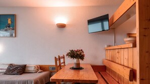 A cozy room with a wooden table, bench seating, a small TV, and a painting on the wall. - Arc 1800: 2-Room Apartment, 6 Persons, Pets Allowed, WiFi (Les Arcs 1800)