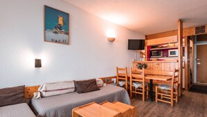 A cozy room with a sofa, a wooden table, and a kitchen area with a microwave and a TV. - Arc 1800: 2-Room Apartment, 6 Persons, Pets Allowed, WiFi (Les Arcs 1800)