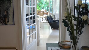 A hallway leading to a living area with a chair, a table, and a vase with flowers. - Deluxe garden level apartment, close to beaches, between Salis and Pinewoods (Antibes)