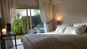 A bedroom with a large bed, a TV on a side table, and a view of greenery outside. - Deluxe garden level apartment, close to beaches, between Salis and Pinewoods (Antibes)