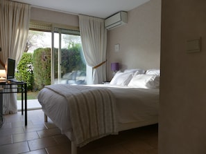 Quarto com cama, escrivaninha com luminária e vista para o verde lá fora.