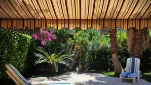 A covered outdoor area with two lounge chairs, a palm tree, and various tropical plants. - Deluxe garden level apartment, close to beaches, between Salis and Pinewoods (Antibes)