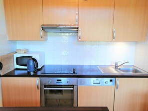 Efficient kitchen with oven, microwave, kettle, and dishwasher, along with ample cabinetry and a stainless steel sink.