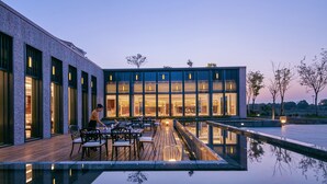 A modern building with a reflective pool, outdoor seating, and a person working at a table.