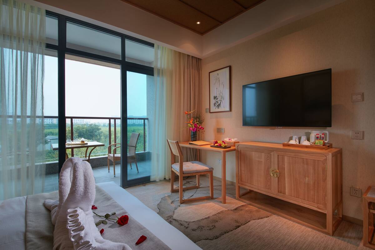 Una habitación de hotel moderna con un ventanal grande, un televisor de pantalla plana, un escritorio de madera y una zona de estar acogedora.
