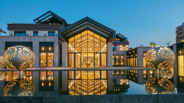 A modern building with a glass facade, a central atrium, and a reflective pool.