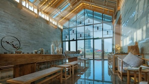 A spacious interior with wooden benches, a high ceiling with skylights, and large windows offering a view of the city.