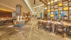 A spacious hotel lobby with a central bar area, wooden furniture, and a modern ceiling design.