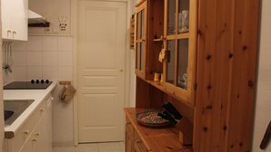 A compact kitchen with white cabinets, a stove, and wooden shelves with glass doors. - Central Apartment in Vars - 3 Rooms, Sleeps 6, Near Slopes & Shops (Vars)