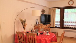 A dining area with a table set for four, a television, and a window with curtains. - Central Apartment in Vars - 3 Rooms, Sleeps 6, Near Slopes & Shops (Vars)
