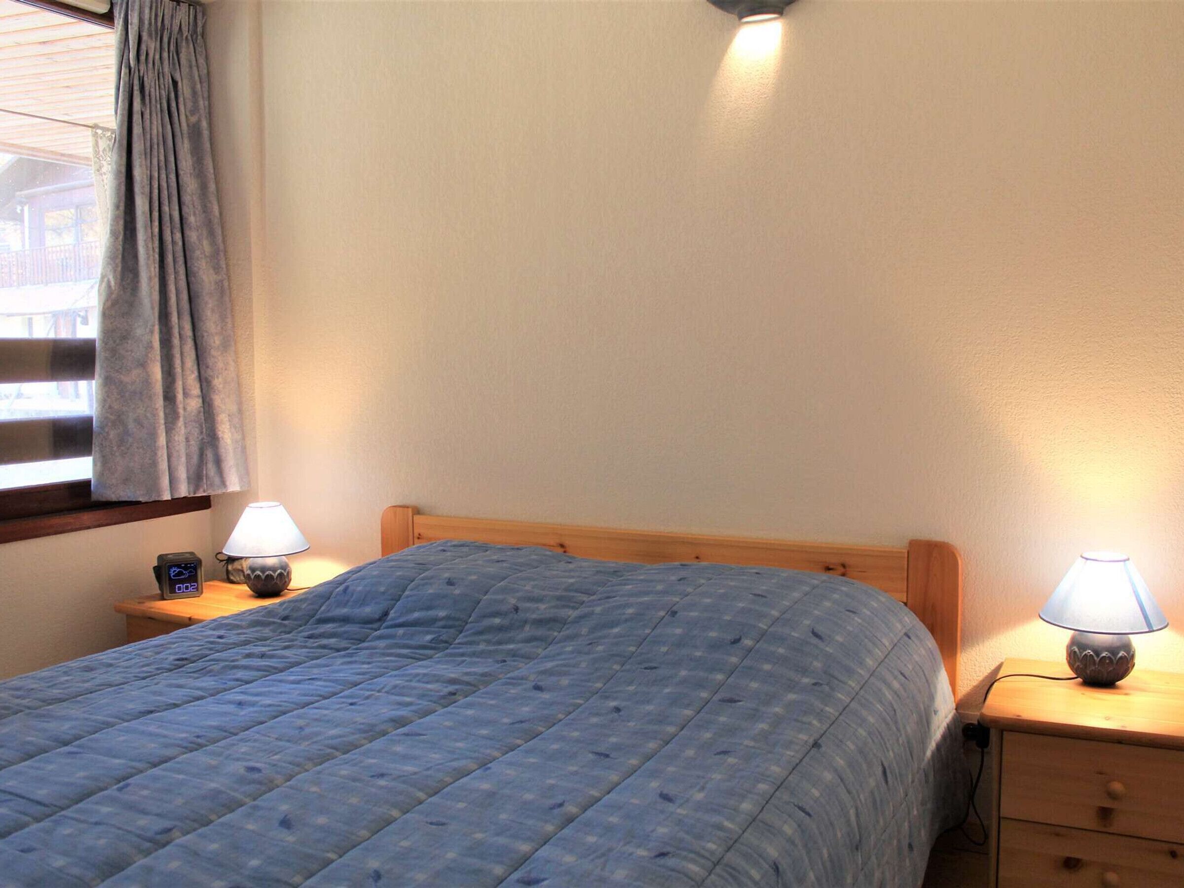 Un dormitorio con una cama, dos mesitas de noche, una lámpara sobre cada una y una ventana con cortinas.