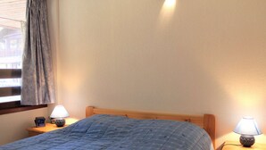 A bedroom with a bed, two bedside tables, a lamp on each table, and a window with curtains. - Central Apartment in Vars - 3 Rooms, Sleeps 6, Near Slopes & Shops (Vars)