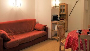 A cozy room with a red sofa, a wooden dining table with a red tablecloth, a cabinet, and a broom leaning against the wall. - Central Apartment in Vars - 3 Rooms, Sleeps 6, Near Slopes & Shops (Vars)