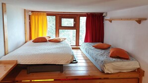 Une petite pièce agréable, dotée de deux lits, d’une fenêtre avec des rideaux et d’un plancher en bois.
