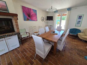 A dining area with a wooden table, white chairs, a television, and a fireplace.