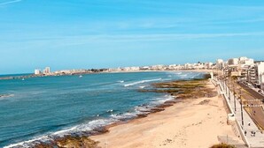 A coastal cityscape with a beach, promenade, and buildings along the shore.