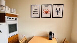 A kitchen with a white stove, a table with a black kettle, and three framed seafood illustrations on the wall.