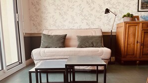 A living room with a sofa, two black-framed tables, a wooden cabinet, and a patterned wallpaper.
