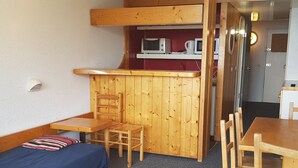 A compact room with a wooden bunk bed, a small wooden table with a chair, a microwave, and a coffee maker on a shelf. - Studio for 5, mountain view, balcony, Arc 1800 (Les Arcs 1800)