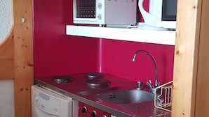 A compact kitchen with a red backsplash, a white stove, a sink, and a microwave on a shelf. - Studio for 5, mountain view, balcony, Arc 1800 (Les Arcs 1800)