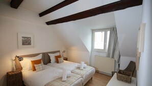 Un dormitorio con dos camas, una ventana con cortinas, un radiador y un cuadro enmarcado en la pared.