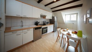 Una cocina moderna con armarios blancos, lavavajillas, microondas y refrigerador. Hay una mesa de comedor con sillas y una ventana que proporciona luz natural.